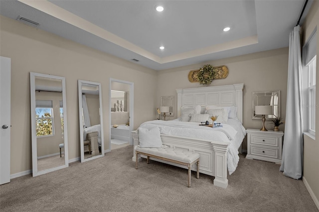 bedroom with a tray ceiling, connected bathroom, and light colored carpet