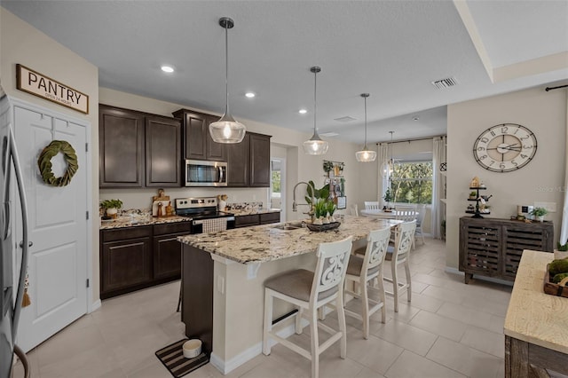 kitchen featuring appliances with stainless steel finishes, sink, hanging light fixtures, a breakfast bar area, and an island with sink