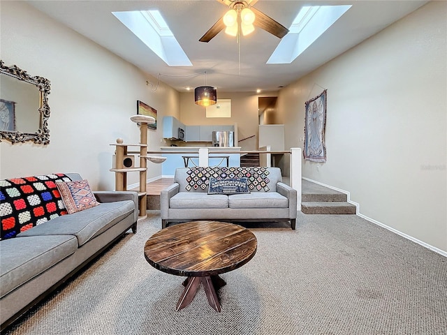 carpeted living room with a skylight, a ceiling fan, and baseboards