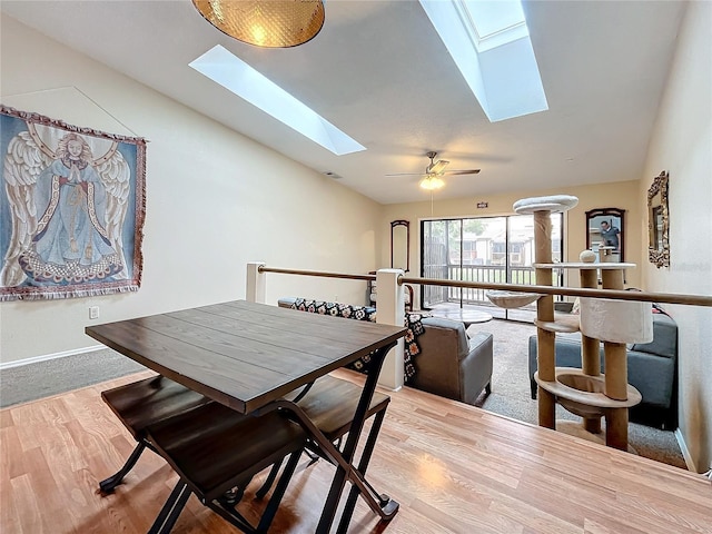 dining space featuring a skylight, vaulted ceiling, wood finished floors, baseboards, and ceiling fan