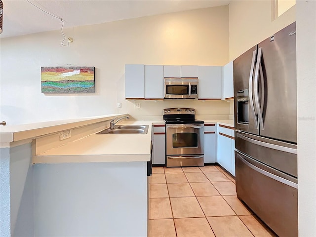 kitchen with appliances with stainless steel finishes, a sink, a peninsula, light countertops, and light tile patterned floors