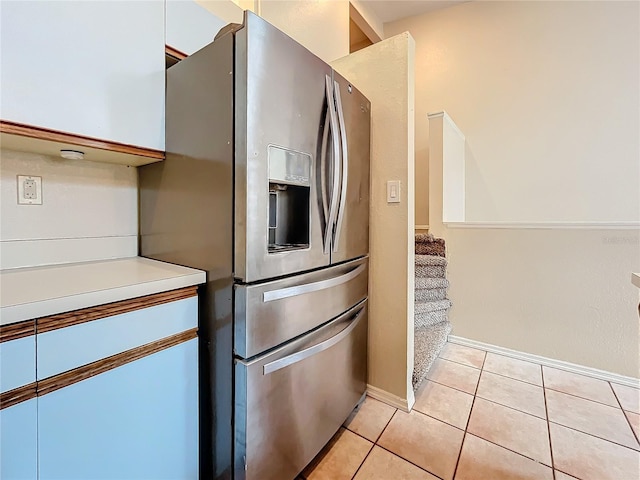kitchen featuring stainless steel refrigerator with ice dispenser, light tile patterned flooring, light countertops, and baseboards