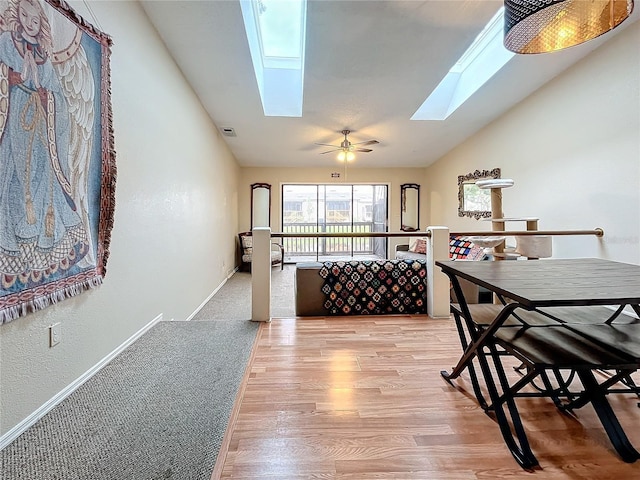 dining room featuring a skylight, lofted ceiling, light wood-style floors, and baseboards