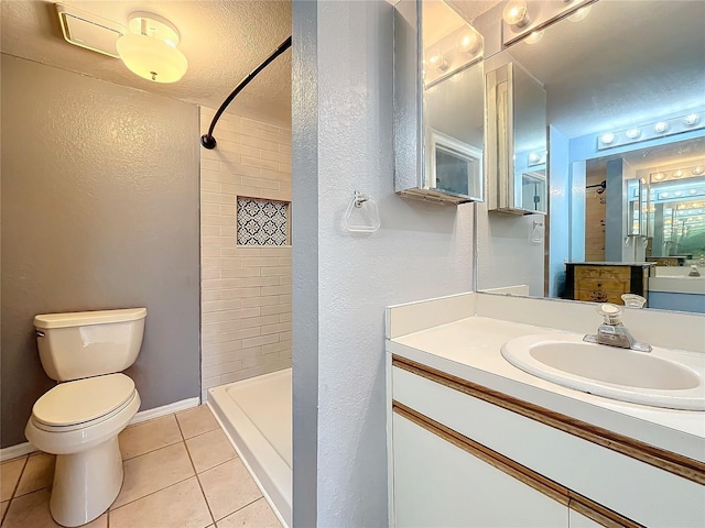 bathroom with tile patterned floors, a tile shower, toilet, vanity, and a textured wall