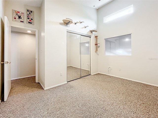 unfurnished bedroom featuring carpet, a closet, baseboards, and a high ceiling