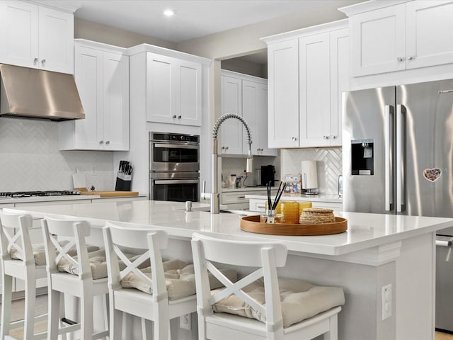 kitchen featuring a kitchen bar, stainless steel appliances, white cabinetry, and a center island with sink