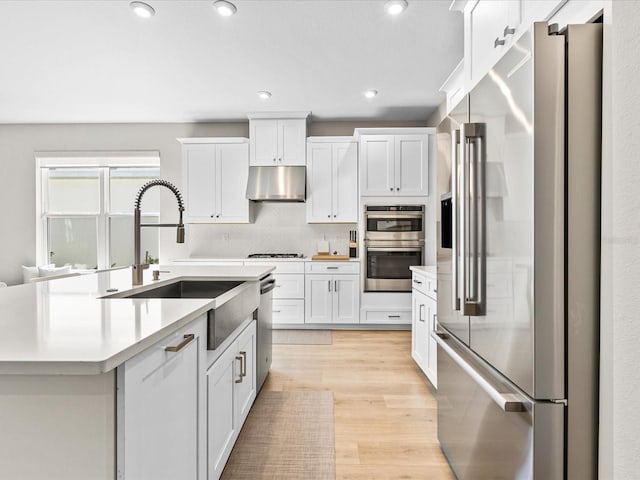 kitchen with white cabinetry, sink, stainless steel appliances, an island with sink, and light hardwood / wood-style floors