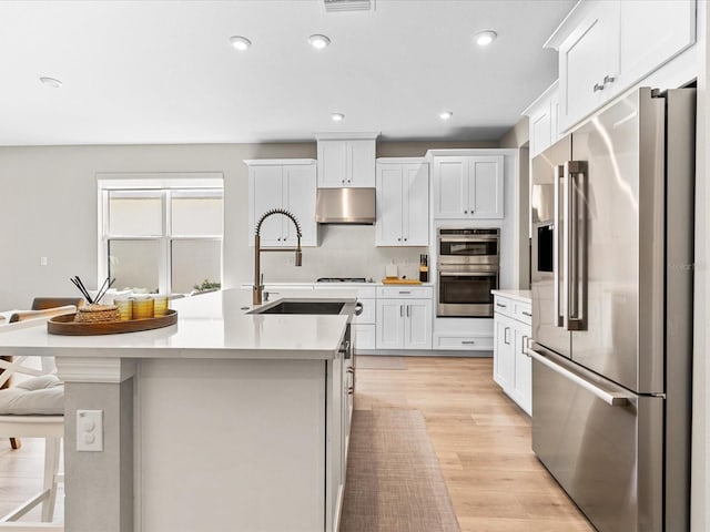 kitchen with white cabinetry, a kitchen island with sink, decorative backsplash, a breakfast bar, and appliances with stainless steel finishes