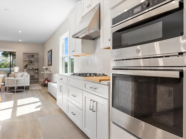 kitchen with tasteful backsplash, light hardwood / wood-style flooring, white cabinets, and appliances with stainless steel finishes