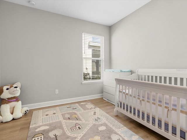 bedroom with wood-type flooring and a nursery area