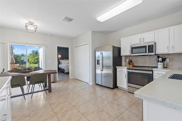 kitchen with white cabinets, decorative backsplash, light tile patterned floors, a notable chandelier, and stainless steel appliances