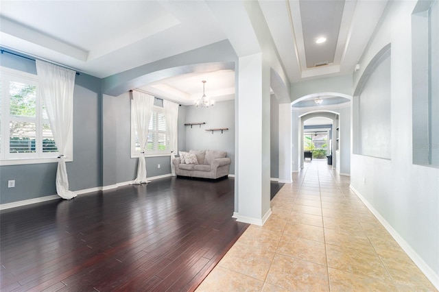 corridor featuring a raised ceiling, a chandelier, and light wood-type flooring