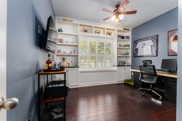 office area with ceiling fan, built in desk, dark wood-type flooring, and a textured ceiling