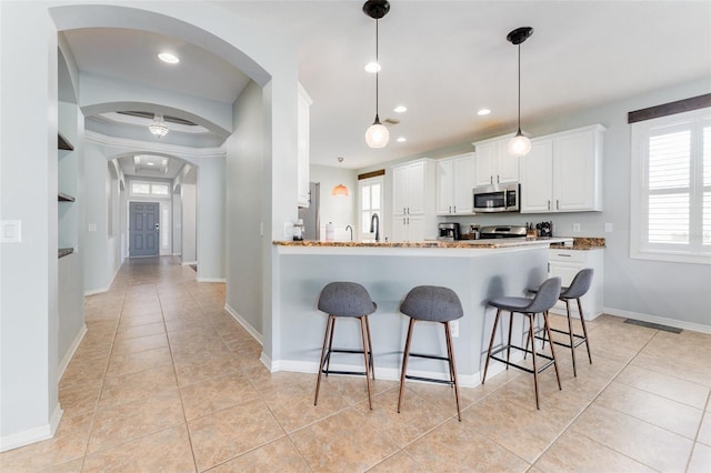 kitchen with kitchen peninsula, stainless steel appliances, light tile patterned floors, decorative light fixtures, and white cabinets