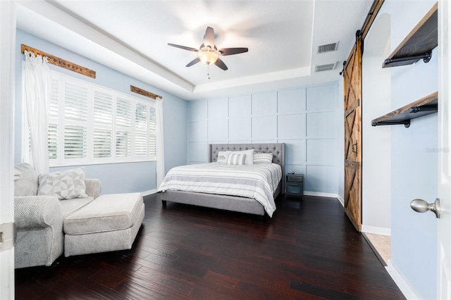 bedroom with dark hardwood / wood-style flooring, a barn door, a raised ceiling, and ceiling fan