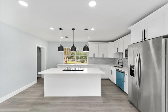 kitchen featuring stainless steel appliances, sink, decorative light fixtures, white cabinetry, and a kitchen island