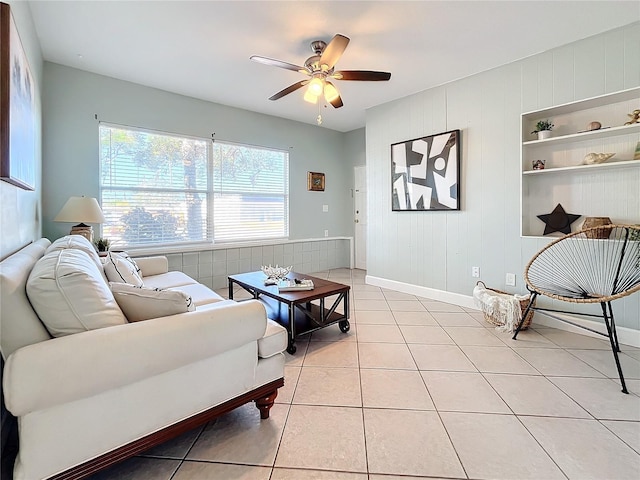 living room featuring ceiling fan, wood walls, light tile patterned floors, and built in shelves