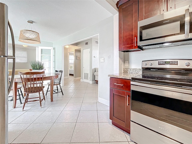 kitchen with pendant lighting, light tile patterned floors, stainless steel appliances, and a textured ceiling