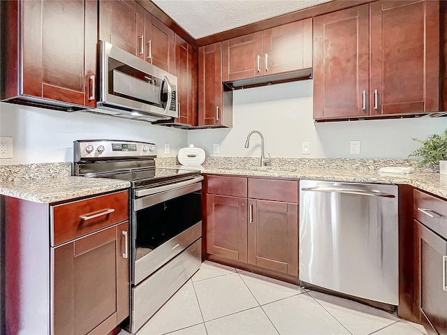 kitchen featuring sink, light stone countertops, a textured ceiling, appliances with stainless steel finishes, and light tile patterned flooring