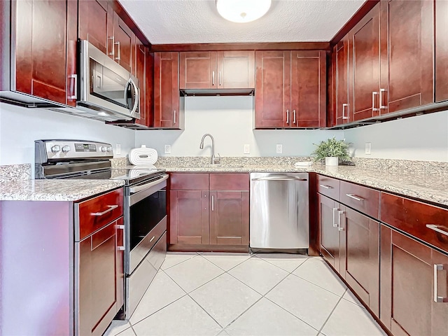516 64th St S, Saint Petersburg, FL 33707 - kitchen featuring stainless steel appliances, a sink, light tile patterned floors, light stone counters, and a textured ceiling