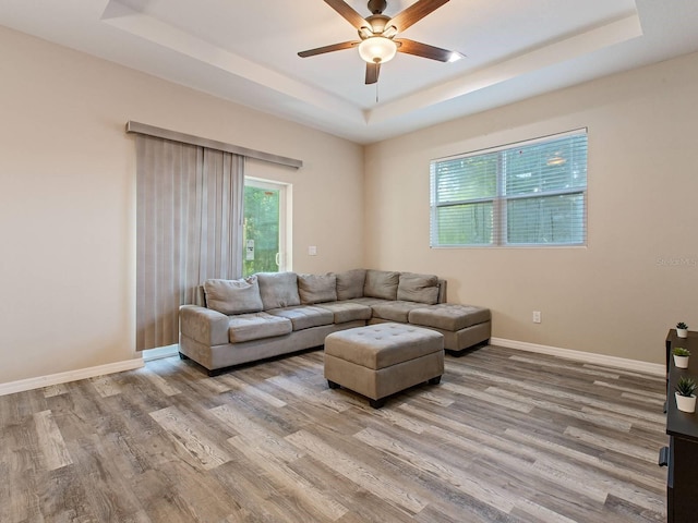 living room with a raised ceiling, ceiling fan, and light wood-type flooring