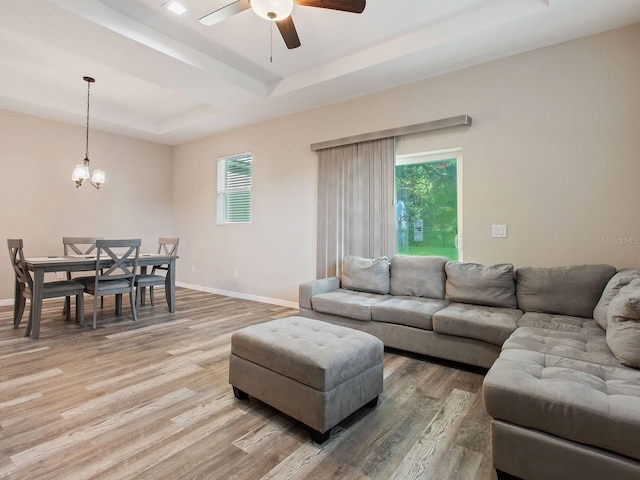 living room featuring hardwood / wood-style floors, ceiling fan with notable chandelier, a raised ceiling, and a healthy amount of sunlight