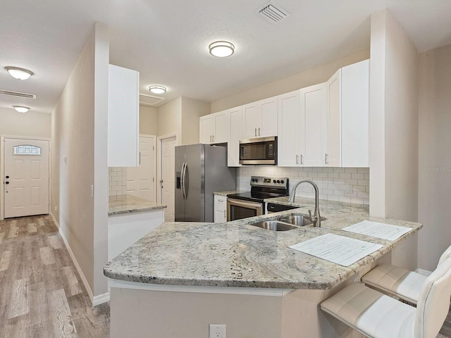 kitchen with white cabinets, a kitchen breakfast bar, sink, appliances with stainless steel finishes, and kitchen peninsula