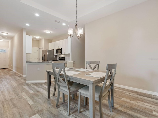 dining space with light wood-type flooring, sink, and a chandelier