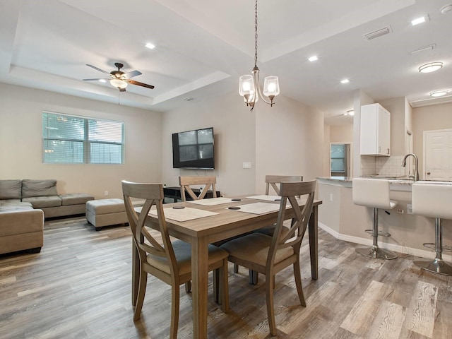 dining space with ceiling fan with notable chandelier, light hardwood / wood-style floors, a raised ceiling, and sink