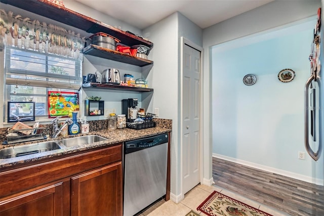 kitchen with stainless steel dishwasher, light tile patterned floors, sink, and dark stone countertops