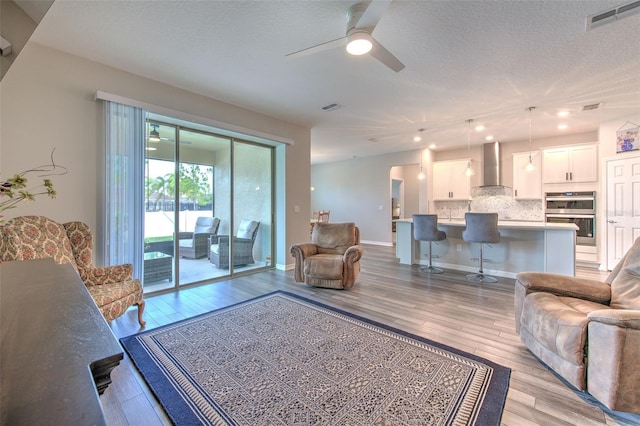 living room with ceiling fan, light hardwood / wood-style floors, and a textured ceiling