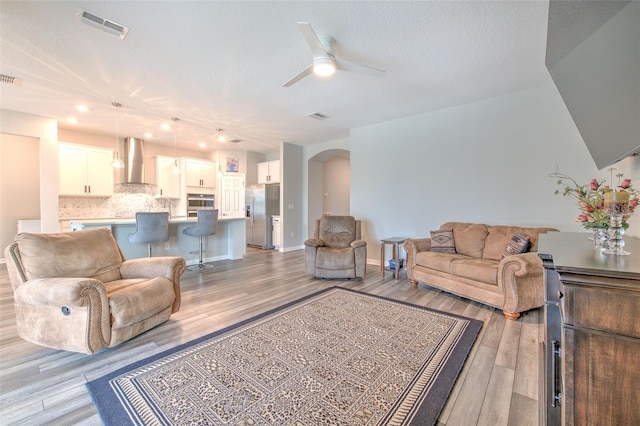 living room with a textured ceiling, light hardwood / wood-style floors, and ceiling fan