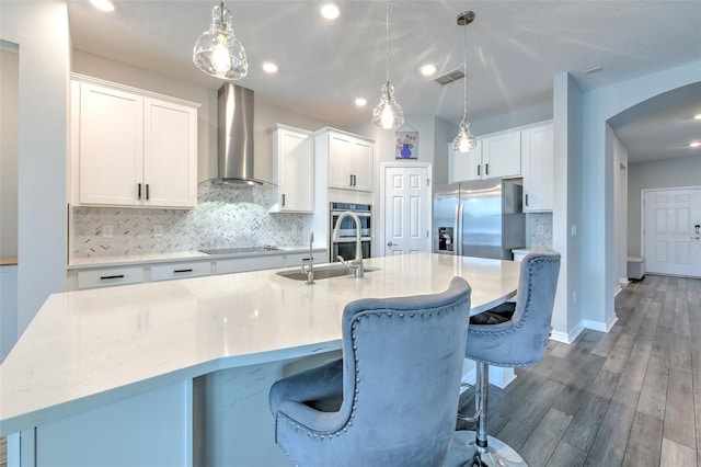 kitchen with dark hardwood / wood-style floors, white cabinetry, wall chimney range hood, and a kitchen island with sink