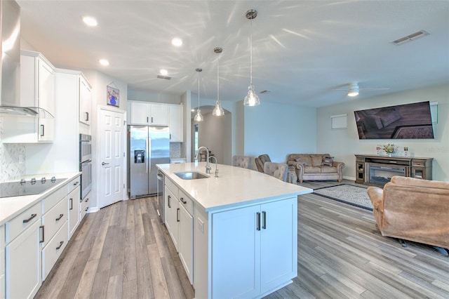 kitchen with pendant lighting, a kitchen island with sink, white cabinets, sink, and stainless steel appliances