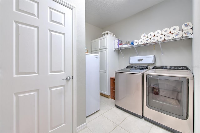 laundry room featuring washer and clothes dryer, light tile patterned floors, and a textured ceiling