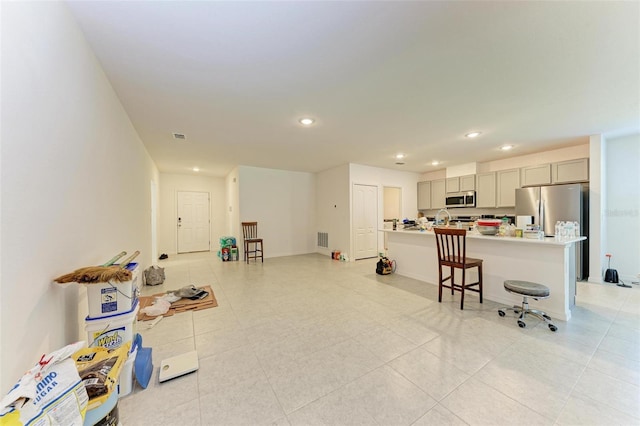 kitchen featuring gray cabinetry, a breakfast bar, stainless steel appliances, light tile patterned floors, and an island with sink