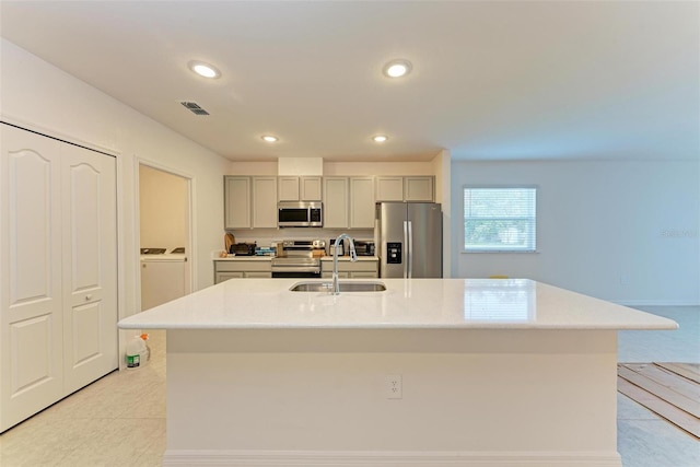 kitchen featuring gray cabinets, sink, an island with sink, and stainless steel appliances