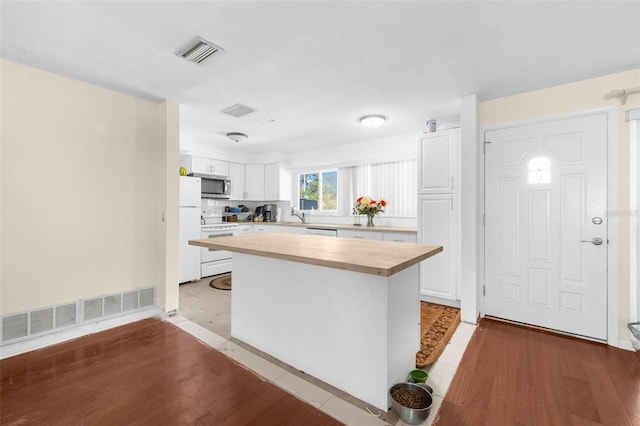 kitchen with wooden counters, white appliances, white cabinets, a center island, and light hardwood / wood-style floors