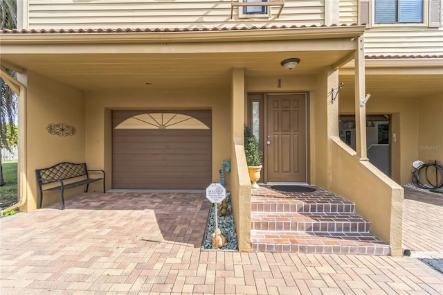 entrance to property with a garage, decorative driveway, and stucco siding