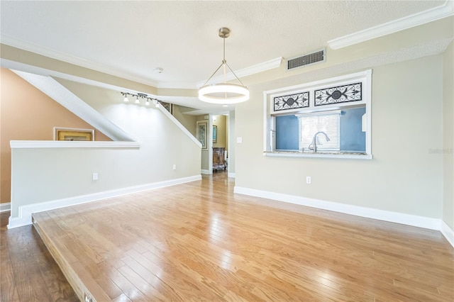 unfurnished living room featuring ornamental molding, visible vents, baseboards, and wood finished floors