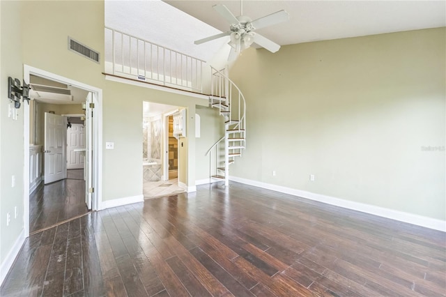 unfurnished living room featuring dark wood-style flooring, visible vents, a towering ceiling, a ceiling fan, and baseboards