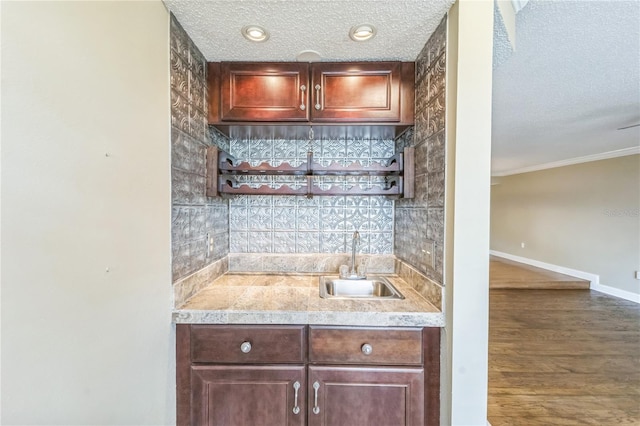 bar featuring a textured ceiling, wood finished floors, a sink, and baseboards