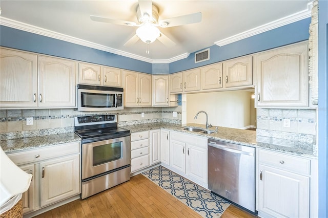 kitchen featuring stainless steel appliances, visible vents, a sink, and ornamental molding