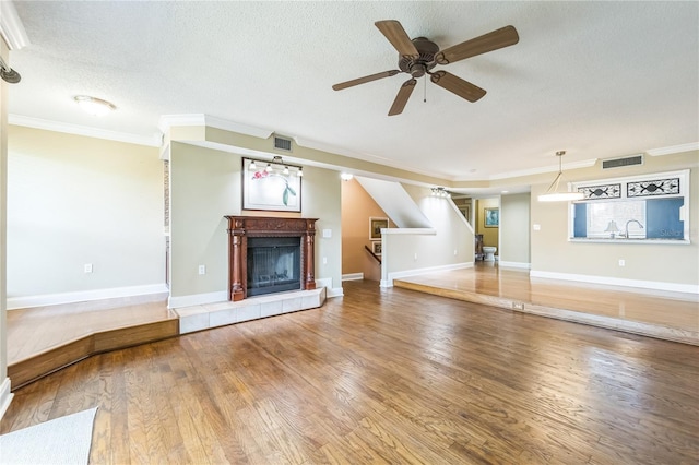 unfurnished living room with a tile fireplace, wood finished floors, visible vents, and stairs