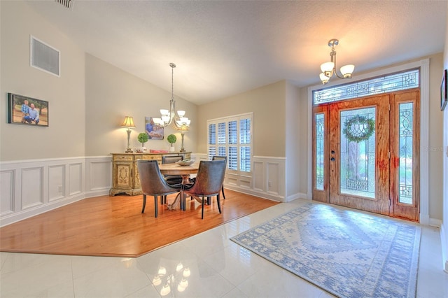 dining space with hardwood / wood-style flooring, a notable chandelier, lofted ceiling, and a textured ceiling