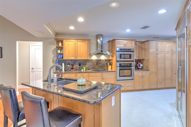 kitchen with tasteful backsplash, wall chimney exhaust hood, stainless steel double oven, sink, and dark stone countertops