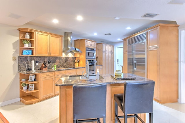 kitchen with a center island with sink, wall chimney range hood, a breakfast bar area, tasteful backsplash, and stainless steel appliances