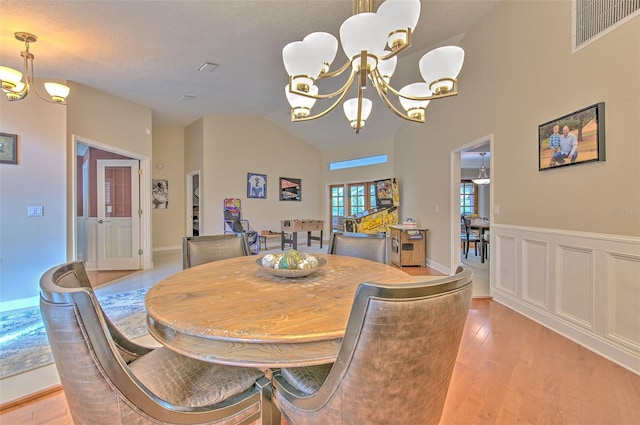 dining area with lofted ceiling, french doors, light hardwood / wood-style flooring, a textured ceiling, and a notable chandelier