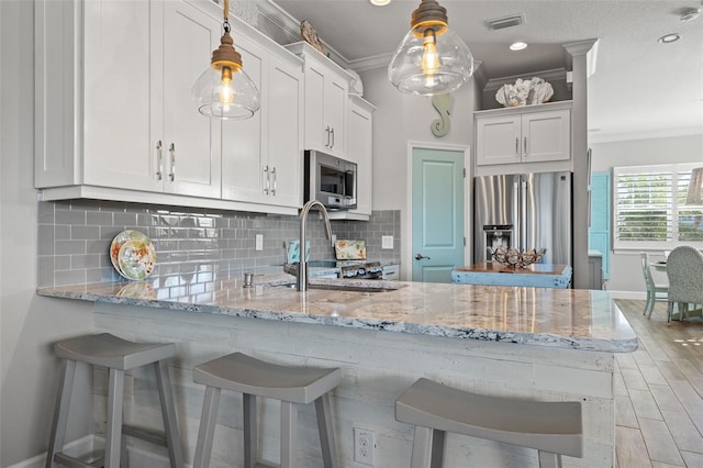 kitchen featuring appliances with stainless steel finishes, white cabinetry, pendant lighting, and a breakfast bar area