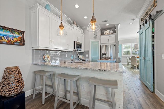 kitchen featuring white cabinets, a barn door, stainless steel appliances, and ornamental molding